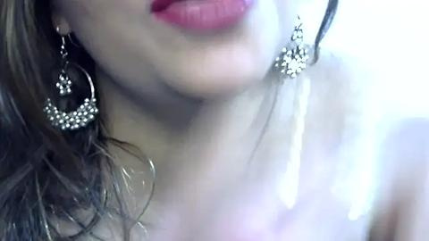 Media: Close-up video of a woman with fair skin, wearing large, sparkly silver hoop earrings and bright red lipstick. The background is out of focus.