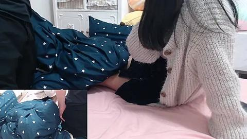 Media: Video of a woman with long black hair, wearing a beige knitted cardigan and black skirt, tucking a teal blanket with white stars into bed in a softly lit bedroom.