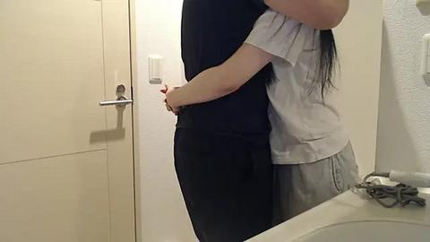 Media: Video of a woman in black pants hugging a woman in light gray pajamas in a bathroom with beige tiles, white sink, and towel rack.