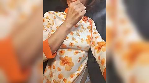 Media: Video of a woman with medium skin tone, wearing a floral-patterned blouse with orange and yellow flowers, her face obscured by smoke. The background is blurred.