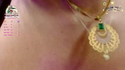 Media: A close-up video of a woman's neck adorned with a delicate gold necklace featuring a large, intricate pendant with a green gemstone. The background is blurred, focusing on the jewelry.