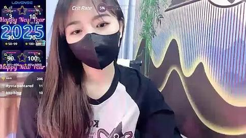 Media: Video of a young Asian woman with long hair, wearing a black face mask, white and black T-shirt, and a background with a \"2021\" digital display and a colorful mural.