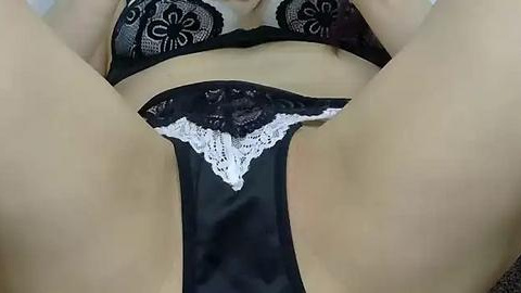 Media: Video of a woman's lower torso, wearing black lace lingerie with white lace trim, lying on her back with legs spread apart, revealing her pubic area.