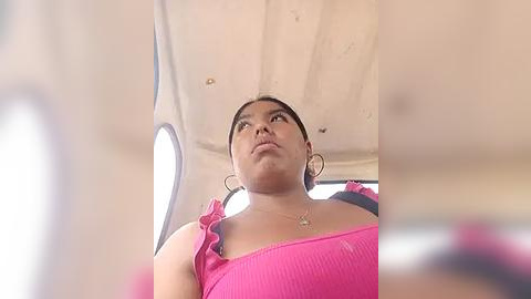 Media: Video of a young woman with dark hair in a pink top, looking upward, seated in a plane.