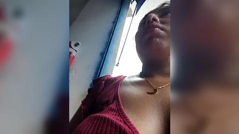 Media: A video of a woman with light brown skin, wearing a red sweater, and a gold necklace, taken from a low angle, inside a bus with blue and white walls.