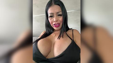 Media: Video of a voluptuous, middle-aged Latina woman with long black hair, wearing a low-cut black dress, showcasing ample cleavage. She has a light brown complexion and wears bright red lipstick. The background is blurred, suggesting a casual indoor setting.