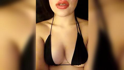 Media: Video of a woman with fair skin wearing a black string bikini, her breasts prominent, lips slightly parted, and the background blurred.