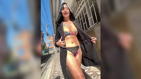 Media: Video of a smiling, curvy Latina woman with long black hair, wearing a colorful bikini, black open jacket, and walking on a sunny, cobblestone street in a city.