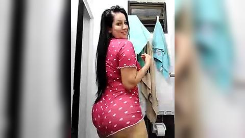 Media: Video of a curvy woman with long black hair in a pink polka-dotted dress, standing in a laundry room, hanging clothes.