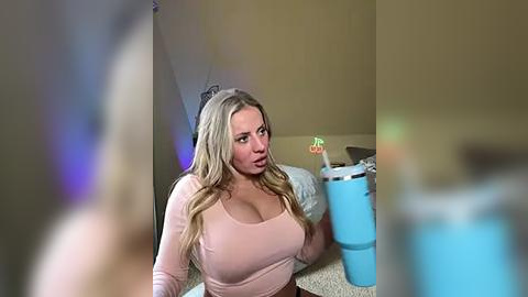 Media: Video of a blonde woman with long hair, wearing a tight pink top, sitting on a beige carpet in a cluttered room with a blue trash can and colorful toys.