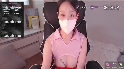 Media: Video of a young Asian woman wearing a pink shirt and mask, seated on a black gaming chair in a dimly lit room. Text overlay reads \"touch me\" and \"love bite.\