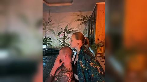 Media: Video of a bald man with tattoos and a woman with glasses, both in bathrobes, in a dimly lit bathroom with tropical wallpaper and potted plants.