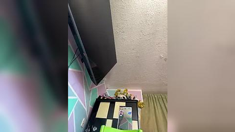 Media: A video of a child's room featuring a black TV mounted on a pink and green geometric-patterned wall, a yellow curtain, and a stuffed animal on a shelf.