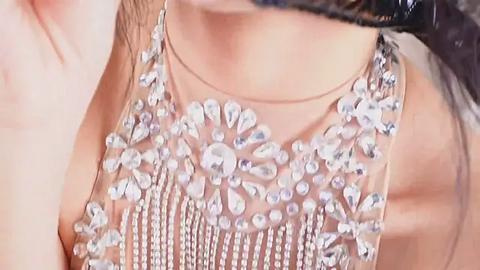 Media: Video of a woman's chest, showing a sleeveless, sheer dress adorned with a beaded, floral design in silver and clear stones. Her skin is light, and her dark hair is partially visible.