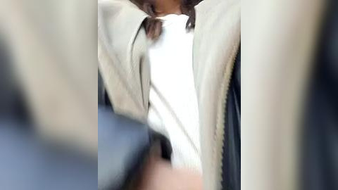 Media: Video of a woman's torso in a beige coat over a white blouse, blurred background, emphasizing texture and color contrast.