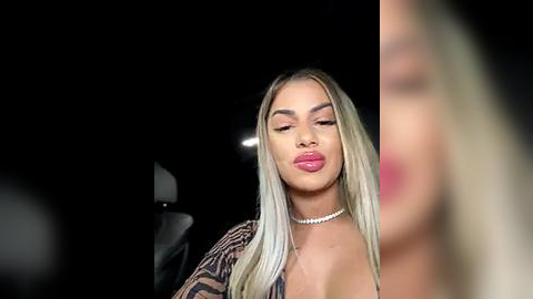 Media: Video of a blonde woman with long, straight hair, wearing a leopard print blouse, pink lipstick, and a choker necklace. She has a confident expression. Dark background.