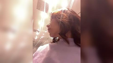 Media: Video of a woman with shoulder-length brown hair in a salon chair, wearing a white cape. The room is softly lit with warm, diffused lighting, creating a cozy atmosphere.