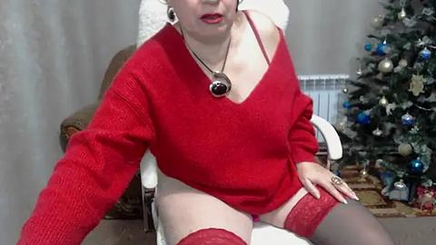 Media: A video of a curvy woman with fair skin, wearing a red off-shoulder sweater, red lace thigh-high stockings, and a necklace, sitting on a chair next to a decorated Christmas tree.