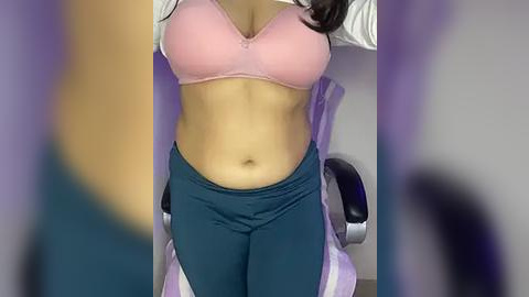 Media: A video shows a light-skinned woman with a fit physique, wearing a pink bra and dark blue leggings, seated in a purple office chair.