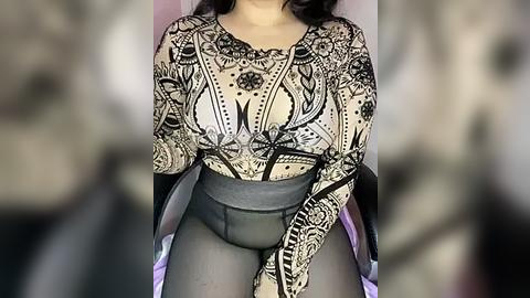 Media: Video of a woman in a sheer, black lace bodysuit with intricate designs, revealing her black bra underneath. She wears black tights, her dark hair visible. Background is blurred.