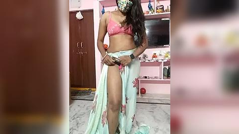 Media: Video of a slender South Asian woman with medium brown skin and long black hair, wearing a pink bra and floral wrap skirt, adjusting a pink thong in a pink-tiled bathroom.