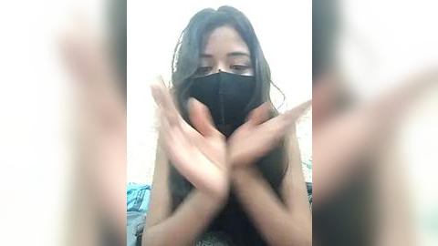 Media: A blurry video of a young woman with long, dark hair and a black face mask, wearing a blue and white striped shirt, hands clasped in front of her face.