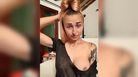 Media: Video of a young woman with light skin and auburn hair, styled in a high ponytail. She has a large tattoo on her left arm and wears a sheer black top exposing her breast.