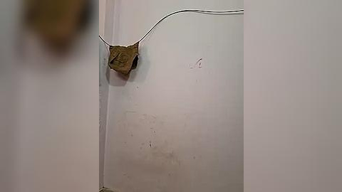 Media: A video of a beige wall with a brown, crumpled paper ball affixed to it by a white cable, suggesting a makeshift repair or installation.