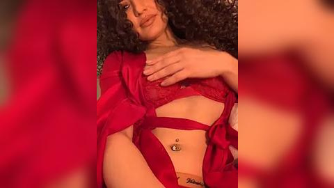 Media: Video of a woman with curly hair, light skin, wearing red lingerie, including a lace bra and satin robe, with a navel piercing.