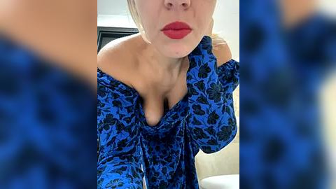 Media: Video of a woman with fair skin, red lipstick, and a blue floral-patterned off-shoulder dress, partially obscured by blurred blue and white patterns.