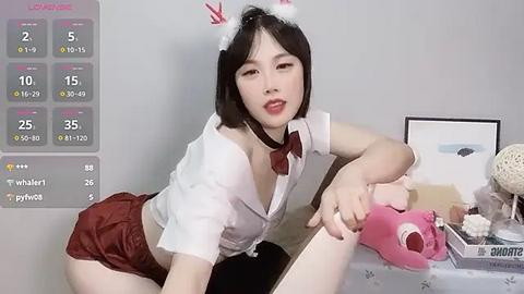 Media: Video of an Asian woman in a white shirt, red skirt, and Santa hat, holding a pink phone, in a room with a table, calendar, and framed picture.