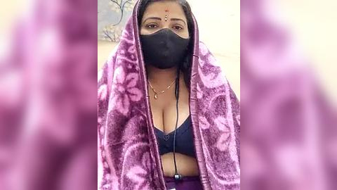 Media: Video of a woman with medium skin tone, wearing a pink shawl, black mask, and a revealing black bra, with blurred background and purple filter.