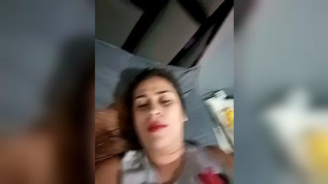 Media: A blurry video of a woman lying on a bed, eyes closed, with a glass of beer in her hand, wearing a red top.