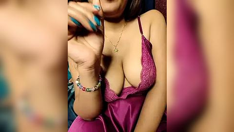 Media: Video of a woman with tan skin, wearing a low-cut, pink satin nightgown with lace trim, revealing ample cleavage, and a colorful beaded bracelet.