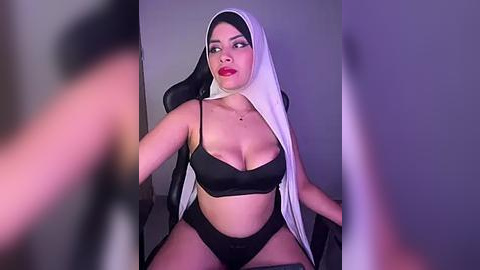 Media: A video of a Latina woman in a black bra and panties, wearing a black and white nun's veil, with a seductive expression, taken from a low angle.