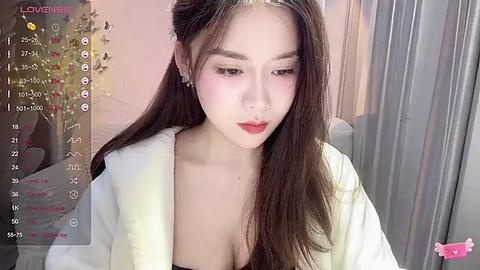 Media: Video of an East Asian woman with long dark hair, fair skin, and red lipstick, wearing a white robe, indoors with curtains and a Christmas tree in the background.