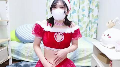 Media: Video of a young East Asian woman in a festive, red Santa-themed outfit with white fur trim, face mask, and a white headband, standing in a bedroom with a bed, curtains, and a white lamp.