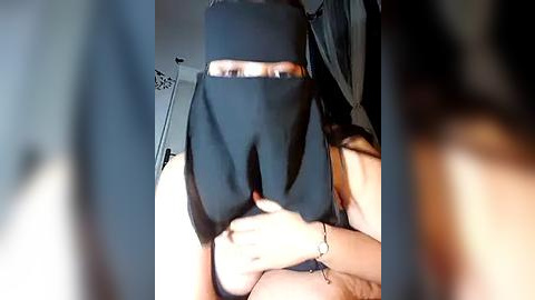 Media: Video of a person wearing a black burqa, partially visible, holding a smartphone with a blurred background. The person's hands and a wrist bracelet are visible.