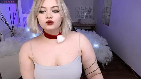 Media: A video of a young woman with short blonde hair, wearing a red Santa hat and a white camisole, with a black thorn tattoo on her arm, standing in a festive, dimly lit room with snowflakes and \"Merry Tips More\" text.