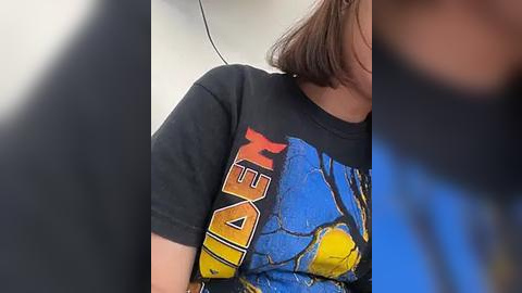 Media: Video of a person wearing a black \"Transformers\" t-shirt with blue and yellow graphics. The person's face is blurred, and the background is out of focus.