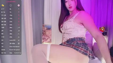 Media: Video of an Asian woman with long black hair, wearing a white lace corset, red plaid skirt, and white thigh-high stockings, reclining provocatively on a bed, in a dimly lit room.