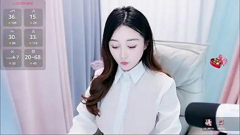 Media: A video of an East Asian woman with long, dark hair, wearing a white blouse, standing in a brightly lit room with pastel-colored curtains.