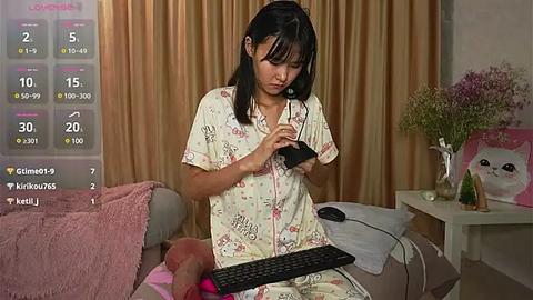 Media: Video of an Asian woman with black hair in pajamas, sitting on a sofa, playing a video game, surrounded by a cozy, decorated living room.