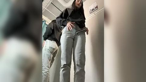 Media: A video of a woman with medium-length hair, wearing a black jacket and light gray jeans, bending down, taken from a low angle.