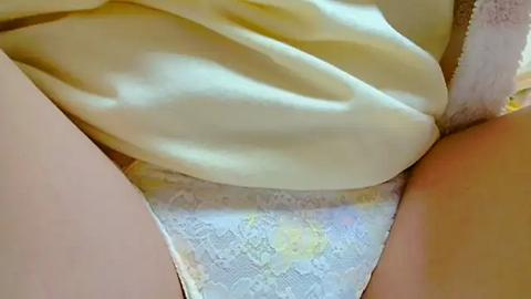 Media: Video of a woman's lower torso, showing her white lace panties partially covered by a yellow shirt. The fabric textures contrast, with the lace's intricate patterns visible beneath the smooth, silky shirt.