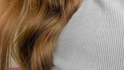 Media: A close-up video shows a person's shoulder with wavy, light brown hair draped over a gray, ribbed sweater. The image focuses on the texture and contrast between the hair and fabric.