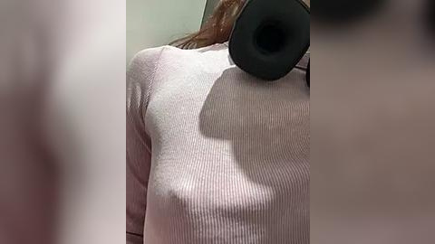 Media: A close-up video of a woman wearing a ribbed, light pink sweater, with a large black over-ear headphone resting on her bare shoulder, casting a shadow.