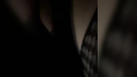 Media: A dimly lit, close-up video shows a woman's bare torso and neck in a dark, low-cut top, emphasizing her cleavage. The background is blurred, enhancing the focus on her skin and the fabric.