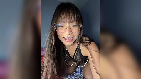 Media: A video of a smiling East Asian woman with long, straight hair, wearing glasses and a black lace bra, with a blurred figure in the foreground.