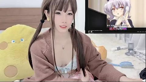 Media: Video of an anime character with long brown hair in a cozy room, wearing a pink cardigan and white lace bra. A TV screen in the background shows a different anime character.